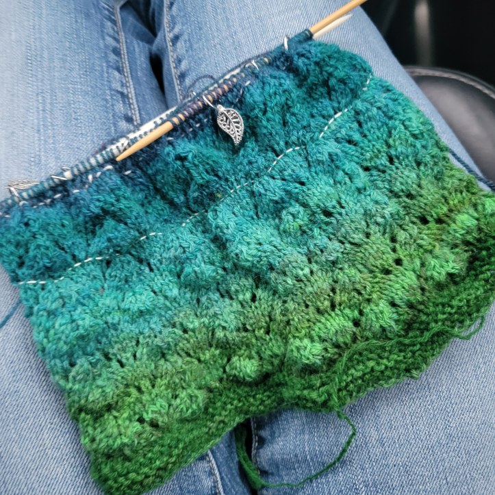 A partially knitted cowl in a denim-clad lap